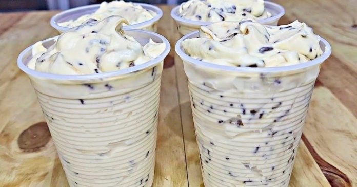 Four cups of vanilla soft-serve ice cream with chocolate chips on a wooden table.