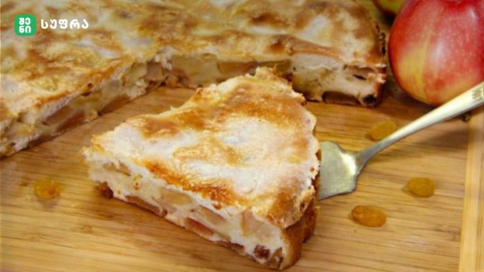 Sliced apple cake on a wooden cutting board with a few raisins nearby.
