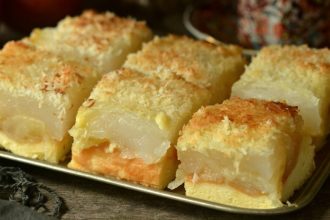 Tray of stacked dessert squares with a pale yellow cake base, an orange filling, a clear gelatin center, and a coconut crumb topping on a metal tray