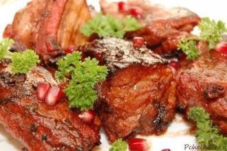 Succulent grilled meat chunks garnished with parsley and pomegranate seeds on a white plate.
