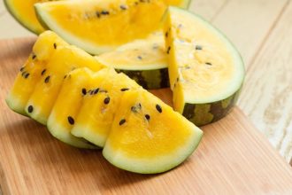 Yellow watermelon wedges with black seeds on a wooden cutting board, showing bright flesh and rind edge