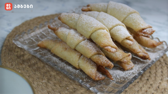 Pile of crescent-shaped pastries dusted with powdered sugar on a glass tray
