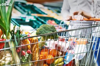 Shopping cart filled with fresh vegetables in a supermarket, with broccoli in the foreground.