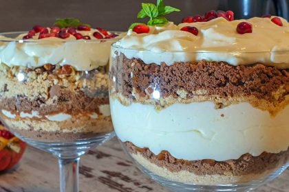 Layered dessert in a glass cup with cream, crumb, and chocolate layers, topped with pomegranate seeds and a mint leaf garnish.